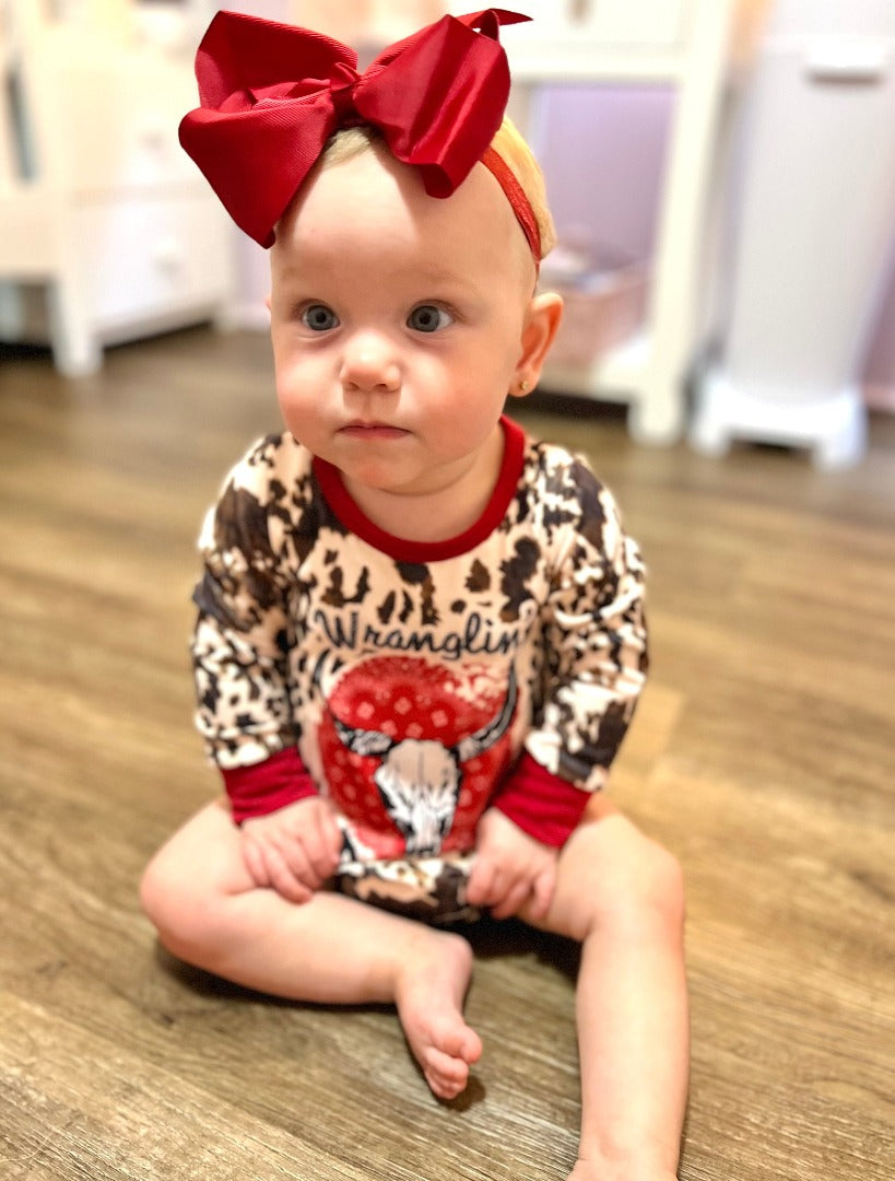 Girls' Wranglin' Babe Onesie: Adorned with a cow animal print and red trim, featuring the phrase 'Wranglin' Babe' and a cattle skull design.