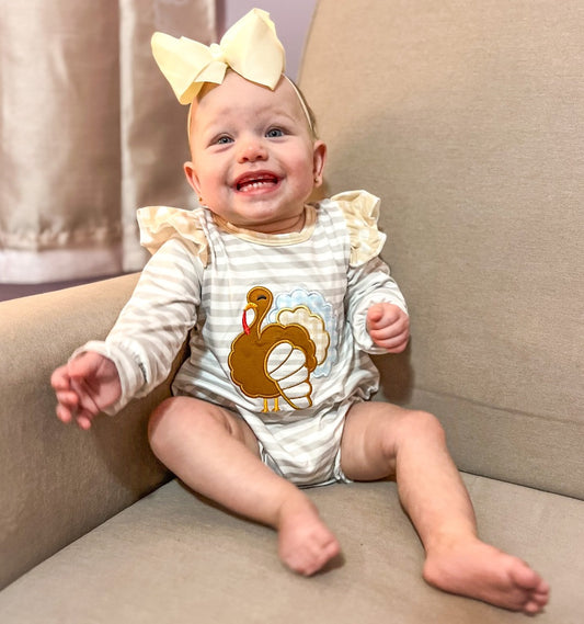 Girls' Miss Gobble Bubble: A white and light grey striped onesie with a prominent turkey motif on the front, accented with light brown ruffles on the shoulders.